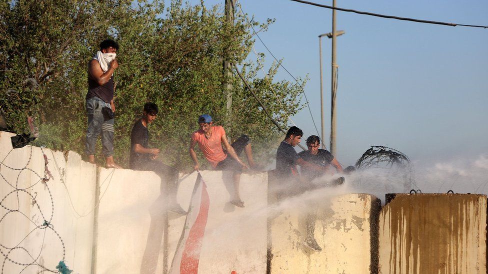Several male protesters climb a wall while facing water cannon