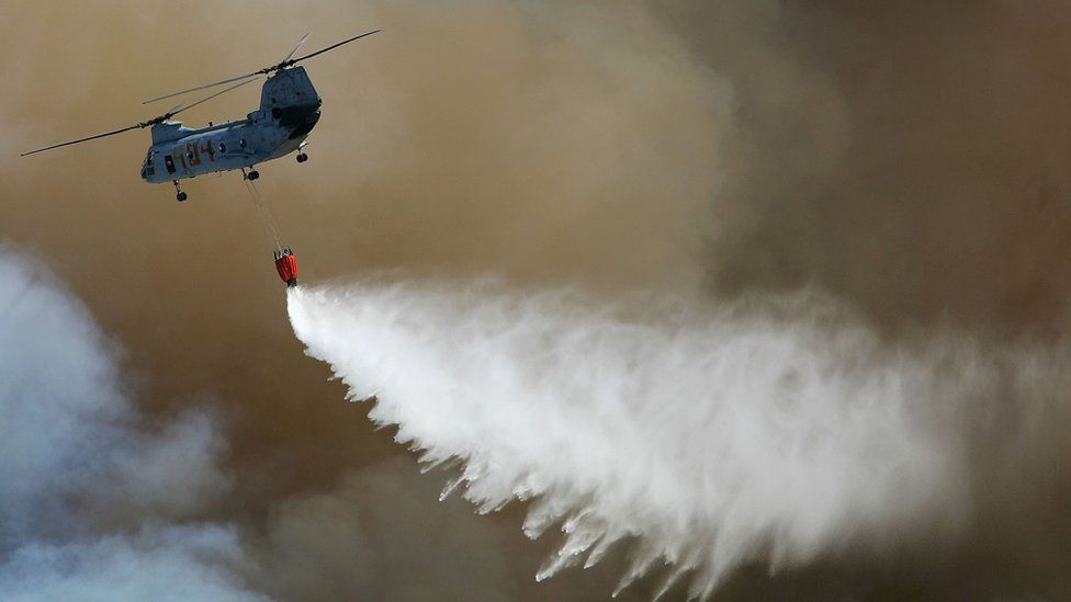 Helicopter flies over a wildfire depositing water