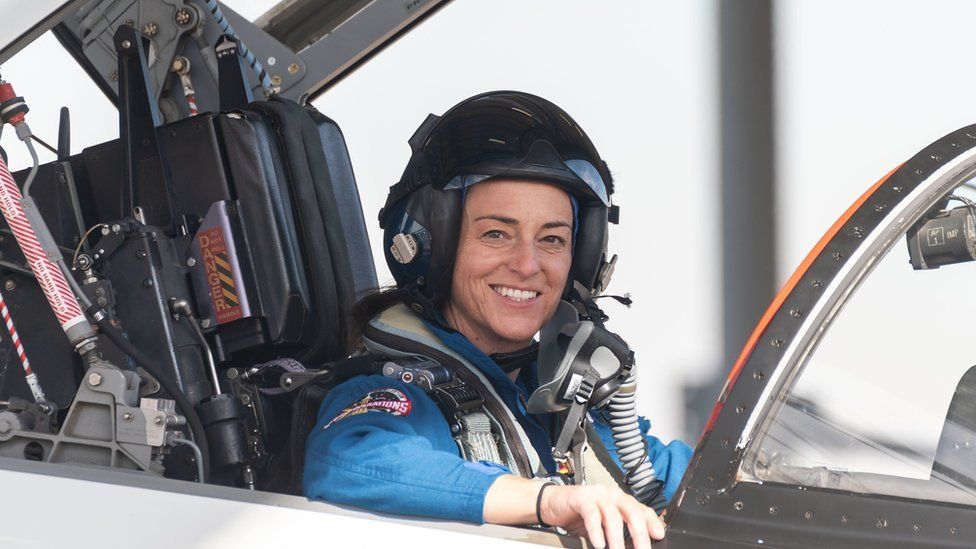 Nicole Mann sits in an aircraft smiling at camera